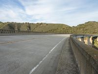 an empty highway near the mountains and bridge at the end of the road as seen from the sidewalk