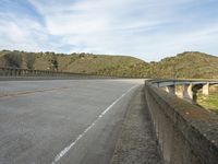 an empty highway near the mountains and bridge at the end of the road as seen from the sidewalk