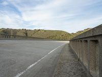 an empty highway near the mountains and bridge at the end of the road as seen from the sidewalk