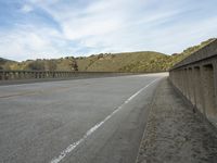 an empty highway near the mountains and bridge at the end of the road as seen from the sidewalk