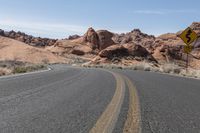 the curve of an empty highway with rock formations in the background of it and sign