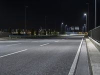 a empty highway in the nighttime on a dark night sky background with several lights, benches and a traffic light at a crossroads