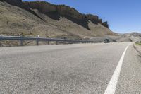 an empty highway near some cliff and a man on his bicycle on the road, near the mountains