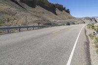 an empty highway near some cliff and a man on his bicycle on the road, near the mountains