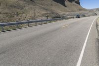 an empty highway near some cliff and a man on his bicycle on the road, near the mountains