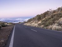 an empty winding road on a mountain with the sun set above the mountains in the background