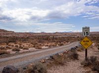 an empty highway in a desert on the side of a dirt road in front of rocks and boulders