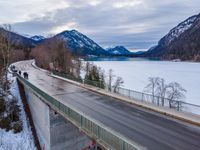 the empty empty highway leads into the mountainside covered in snow and trees with some frozen water