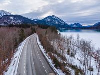 the empty empty highway leads into the mountainside covered in snow and trees with some frozen water