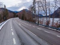 the empty empty highway leads into the mountainside covered in snow and trees with some frozen water