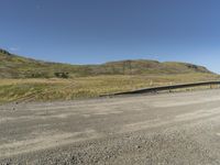 an empty highway with some hills in the distance at one side and some mountains in the distance