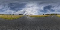 a photo of a wide empty highway with sky in background and clouds hovering overhead of road with two empty roads