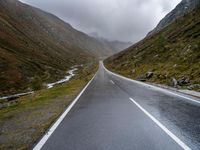 a narrow highway is empty and steep ahead of the road sign with a cloudy sky behind