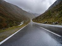 a narrow highway is empty and steep ahead of the road sign with a cloudy sky behind