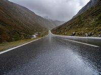 a narrow highway is empty and steep ahead of the road sign with a cloudy sky behind