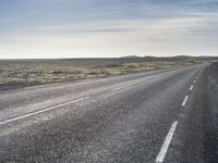 a lone, long empty highway with no traffic on it, stretching across a field