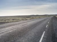 a lone, long empty highway with no traffic on it, stretching across a field