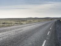 a lone, long empty highway with no traffic on it, stretching across a field