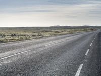 a lone, long empty highway with no traffic on it, stretching across a field