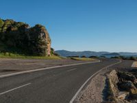 empty highway with steep hills in the background on sunny day, near ocean with beach