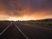 an empty highway during the sunset with mountains in the background and clouds in the sky