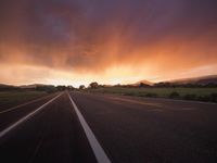 an empty highway during the sunset with mountains in the background and clouds in the sky