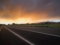 an empty highway during the sunset with mountains in the background and clouds in the sky