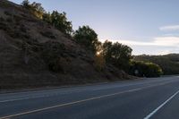 an empty highway with a stop sign in the sunset light behind it and a forest in the distance