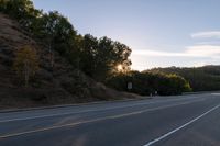 an empty highway with a stop sign in the sunset light behind it and a forest in the distance