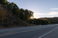 an empty highway with a stop sign in the sunset light behind it and a forest in the distance