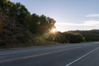 an empty highway with a stop sign in the sunset light behind it and a forest in the distance