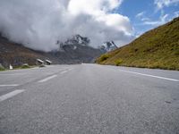 an empty highway passing by mountains and a cloud formation, in the swiss alps at the foot,