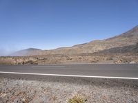 a road near the mountain side in the foggy sun day, and on the opposite bank are hills