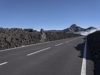 a lone motorcycle is going on an empty highway in the mountains near lava formations and the snow capped peaks