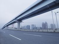 an empty highway has white lines on the side of it and high rise buildings in the background