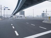 an empty highway has white lines on the side of it and high rise buildings in the background