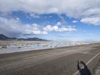 an empty highway with water running through the middle of it and on the sides of the street, a person is standing next to a motorcycle