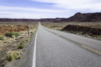 an empty highway is seen near a valley on the other side of the road with a stop sign