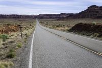 an empty highway is seen near a valley on the other side of the road with a stop sign