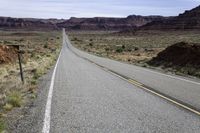 an empty highway is seen near a valley on the other side of the road with a stop sign