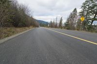 a highway is empty with two yellow signs on both sides of it, along with trees and bushes on both sides,