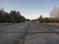 an empty highway on the outskirts of wooded area in the sun set setting, looking at a small yellow fire hydrant