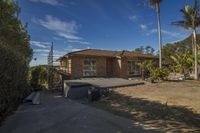 an empty house with lots of windows and landscaping in front of it at the top of the road, palm trees on either side