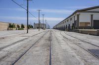 a long empty street with an empty building behind it and a train track on the one side