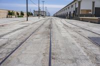 a long empty street with an empty building behind it and a train track on the one side