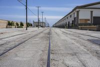 a long empty street with an empty building behind it and a train track on the one side