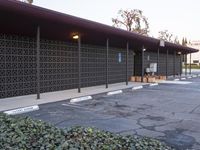 an empty parking lot with benches and plants on the side of it and buildings behind