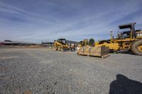 two construction vehicles sitting parked in an empty lot, and the one behind them is taking off its load