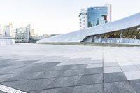 this is an empty and modern public plaza with modern architecture in the background, including a huge white building with windows