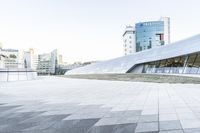 this is an empty and modern public plaza with modern architecture in the background, including a huge white building with windows